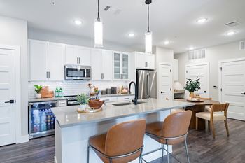an open kitchen and dining area with white cabinets and a marble counter top